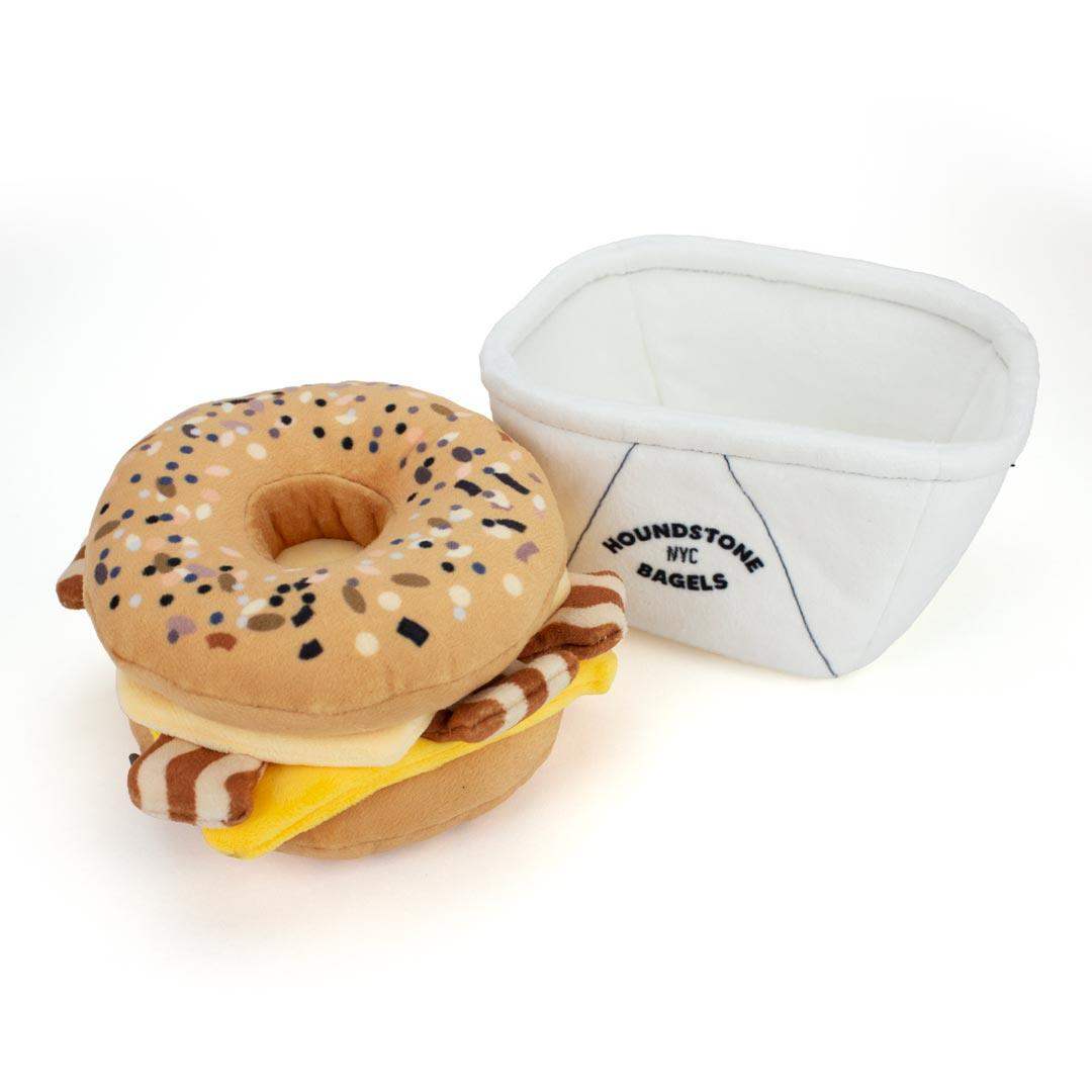 Plush bagel with cream cheese and a dog toy box labeled 'Houndstone NYC Bagels' on a white background