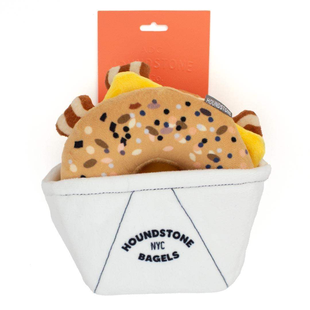 interactive Dog toys shaped like a bagel in a basket with 'Houndstone NYC Bagels' branding on a white background.
