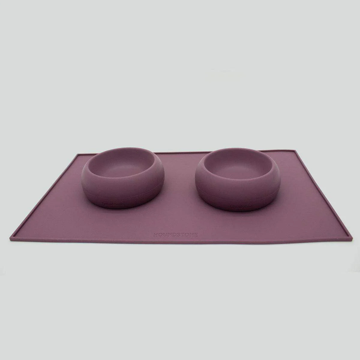 Purple dog bowls set on a matching dog food mat with a plain background