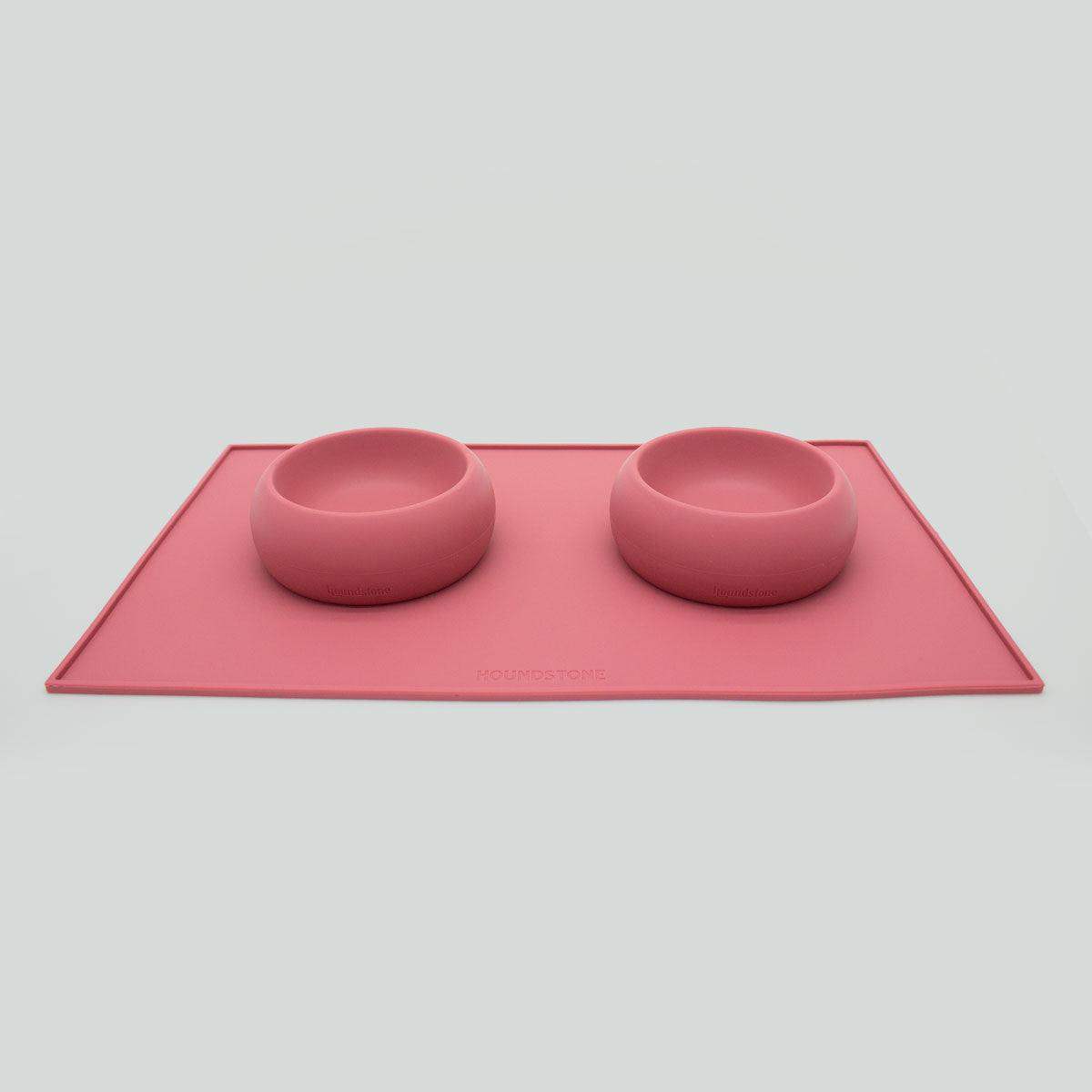 Pink silicone mat with two dog bowls on a light gray background