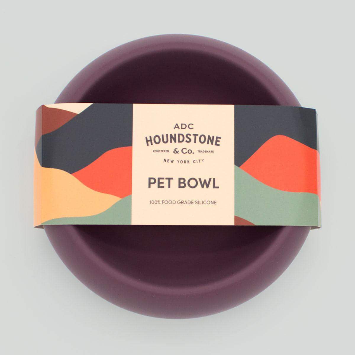 Purple dog bowl with a branded packaging label on a light gray background