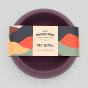 Purple dog bowl with a branded packaging label on a light gray background